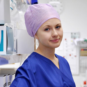 En kvinnlig anställd tittar in i kameran och har en operationsmössa på huvudet